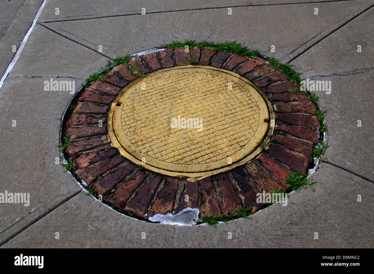 Man hole cover decorated to look like a flower with yellow center and bricks for orange petals in Fort Wadsworth, Staten Island Stock Photo