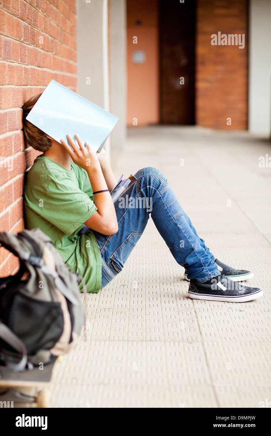 frustrated high school boy using book cover his face in school passage Stock Photo