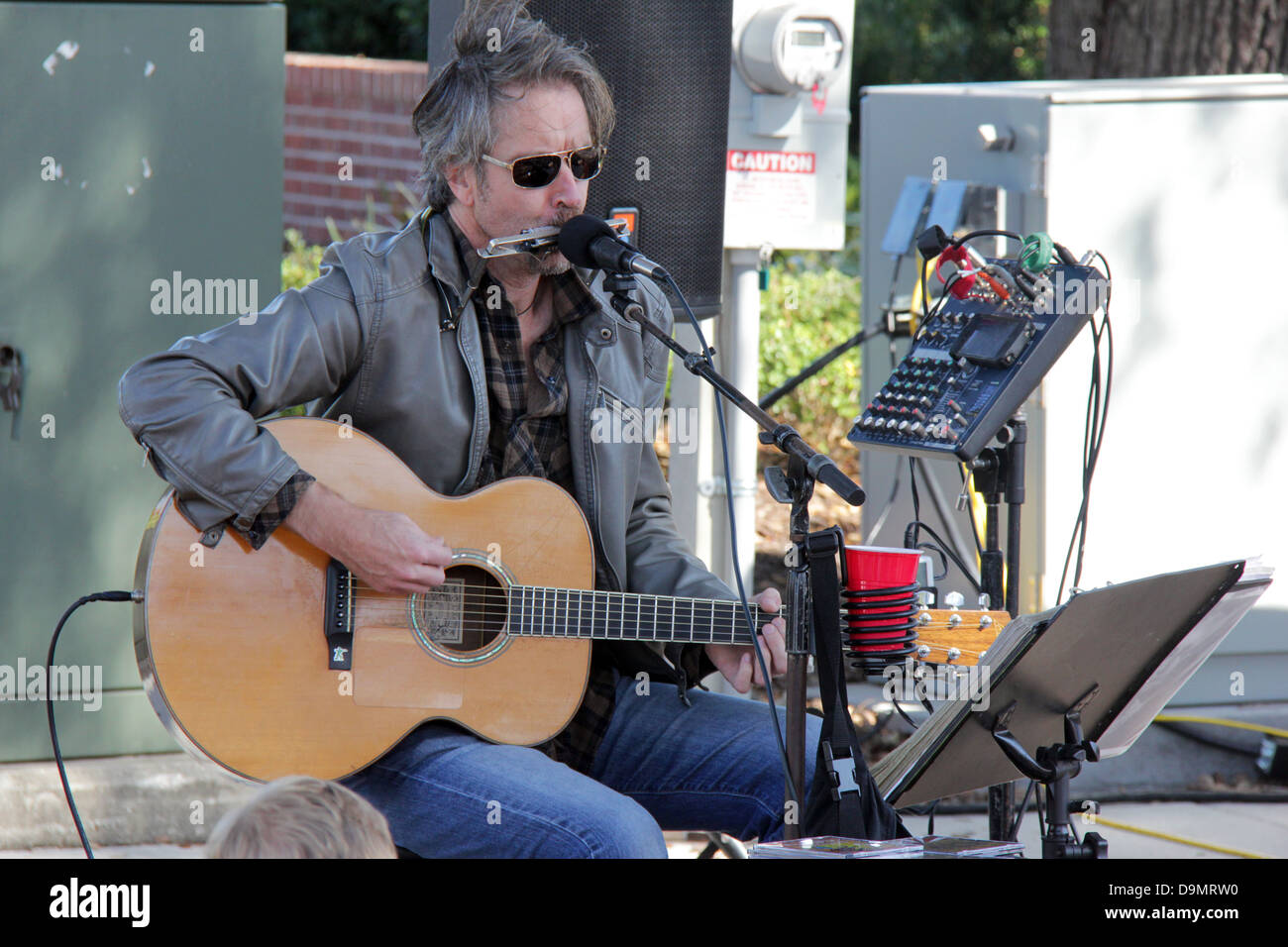 A man playing the harmonica and a guitar in a public presentation Stock