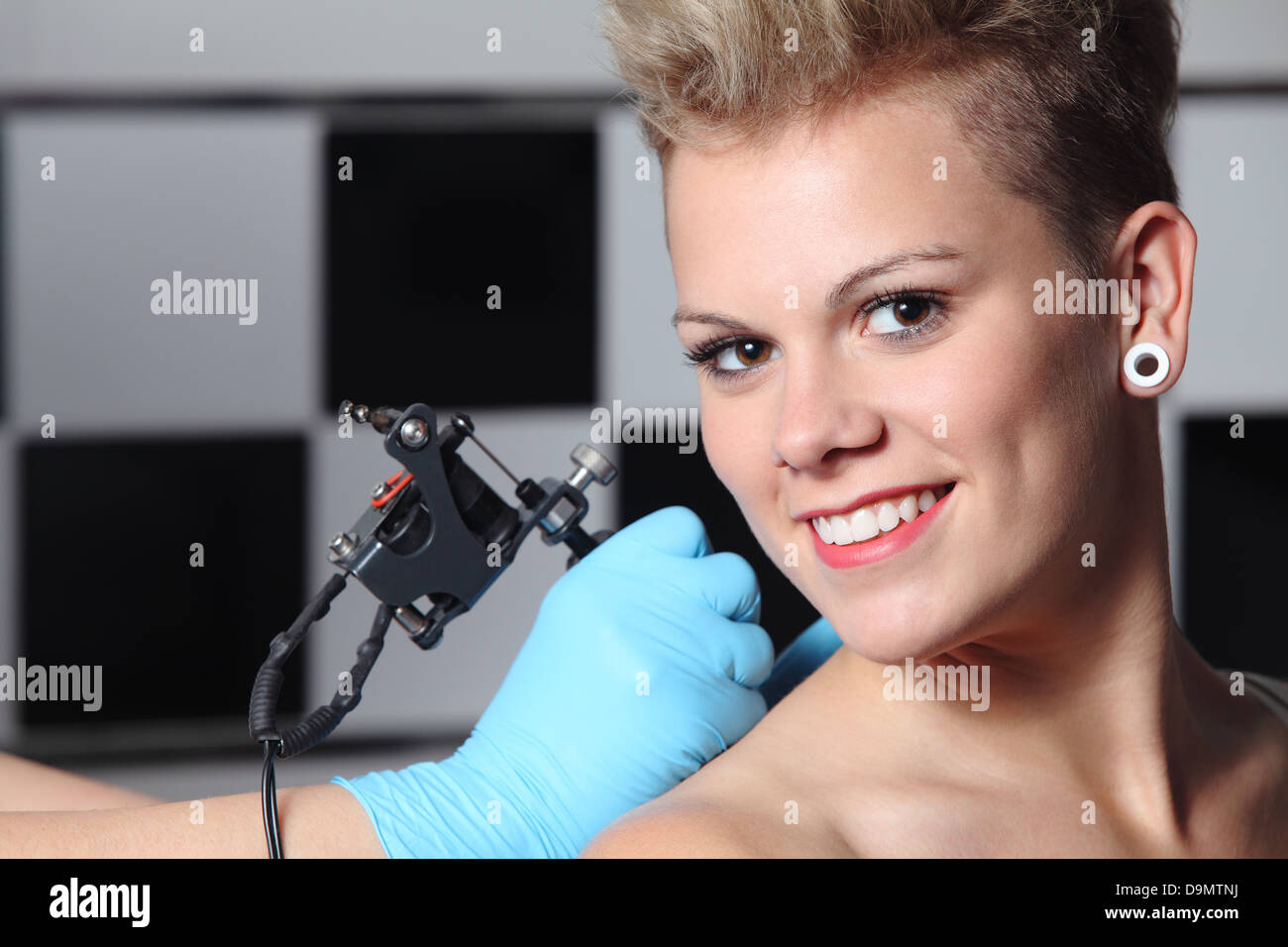 Beautiful woman looking at camera while somebody is making a tattoo on her shoulder Stock Photo