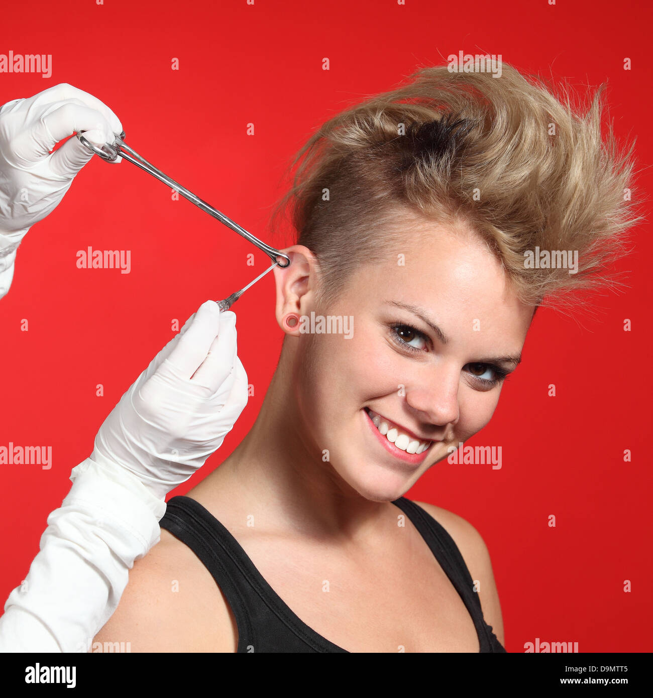 Professional hands making a piercing hole to a fashion woman on a red background Stock Photo