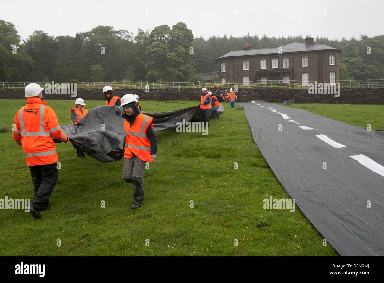 20 activists dressed in roadbuilders' high viz clothing and hard hats roll out a fake road in the field  immediately below Crag Hall, Cheshire in who's  grounds  the Chancellor  of the  exchequer George Osbornes has a residence .   The protest was made to highlight the expected  release of money for roadbuilding schemes throughout  the UK in the imminent spending  reivew on Wednesday 26th June Stock Photo