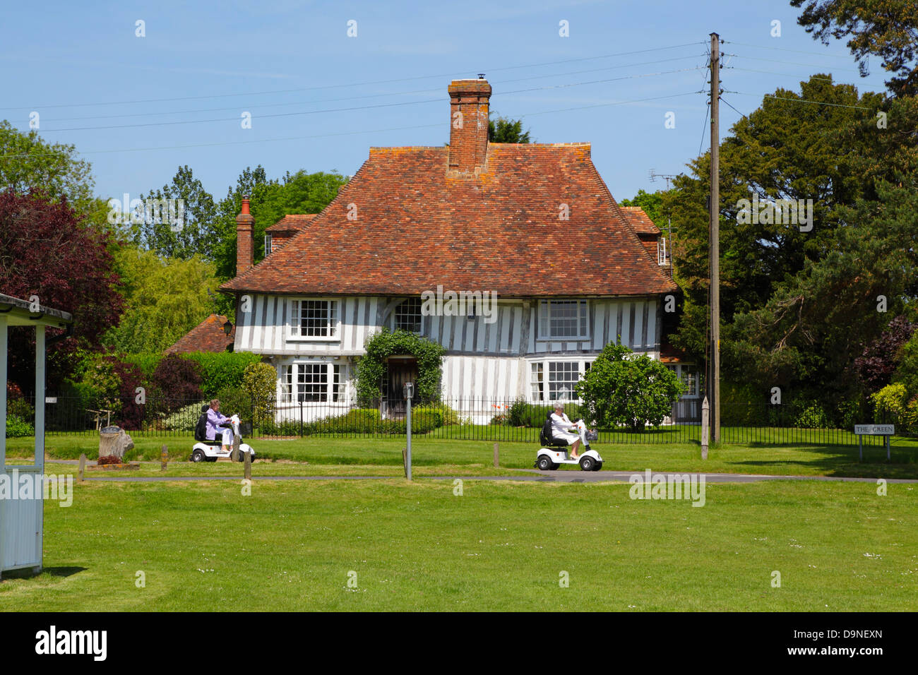 Two ladies on mobility scooters riding along The Green, Woodchurch England Kent UK GB Stock Photo