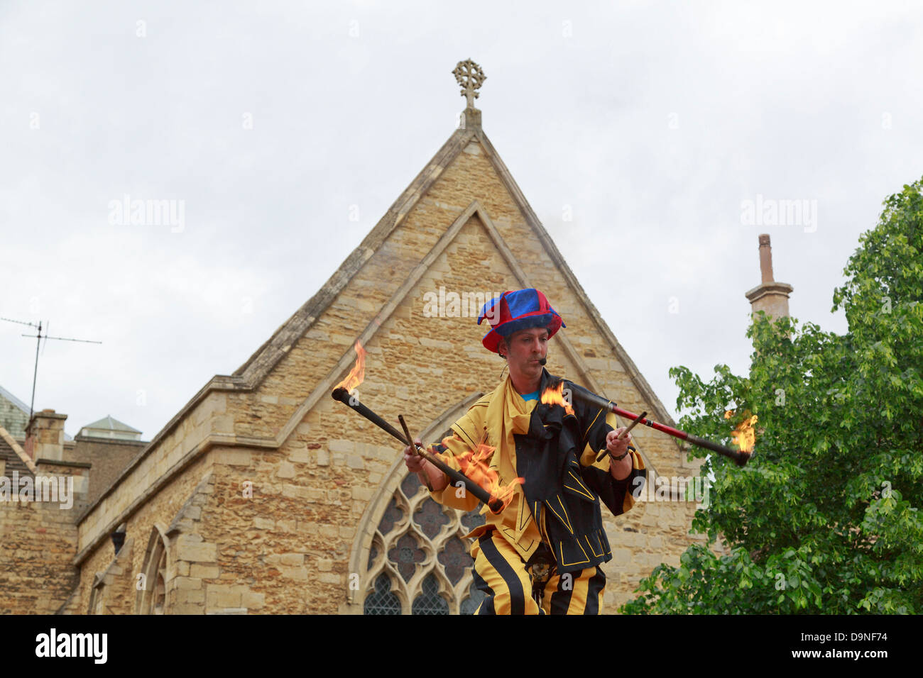 Jester riding a tall unicycle and juggling sticks with fire, Peterborough Heritage Festival 22 June 2013, England Stock Photo