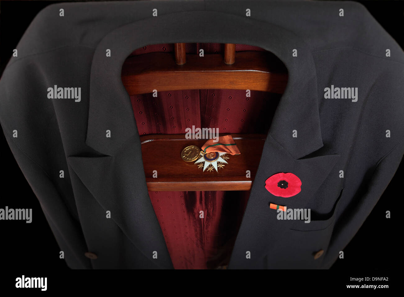 A suit jacket is placed on the jack. A poppy is attached to the lapel and various medals are placed on the rack . Low key Stock Photo