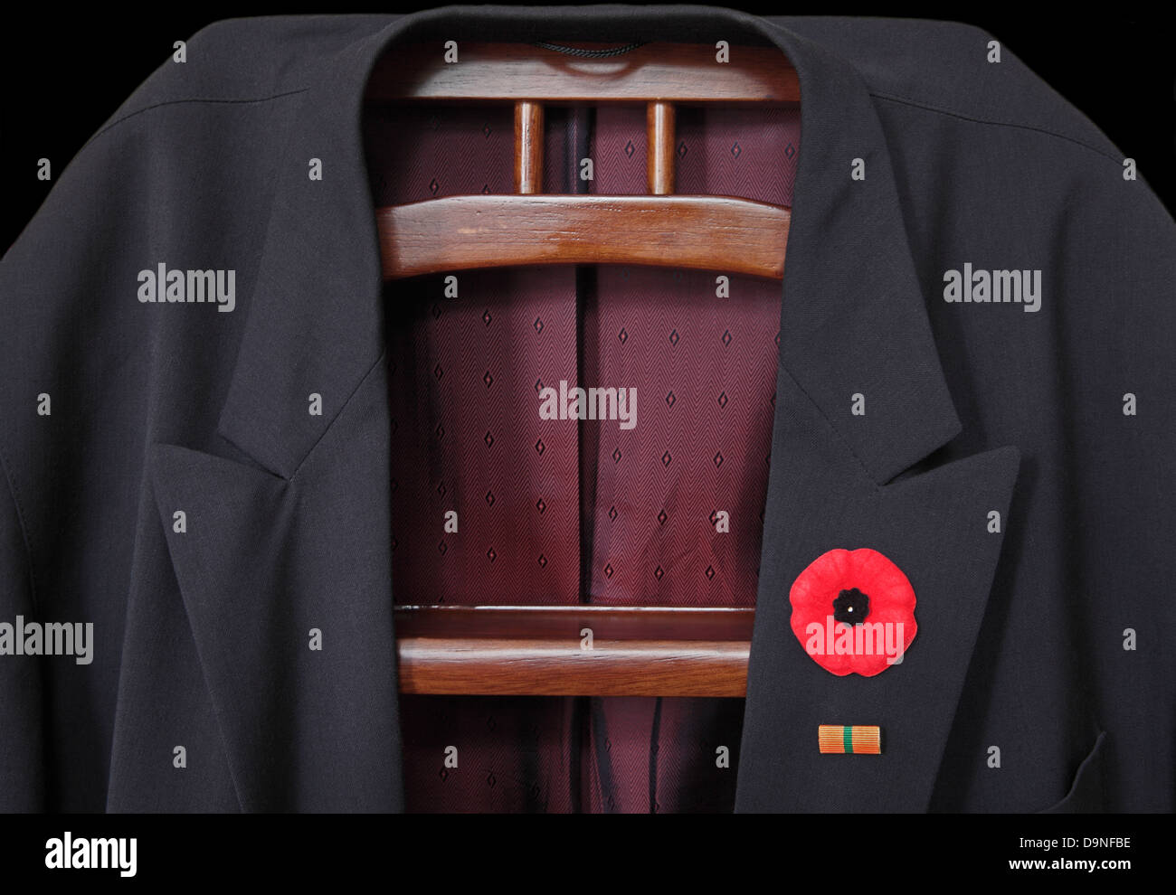 A suit jacket is placed on the jack. A poppy is attached to the lapel with a military recall barrette pinned beneath it  Low key Stock Photo