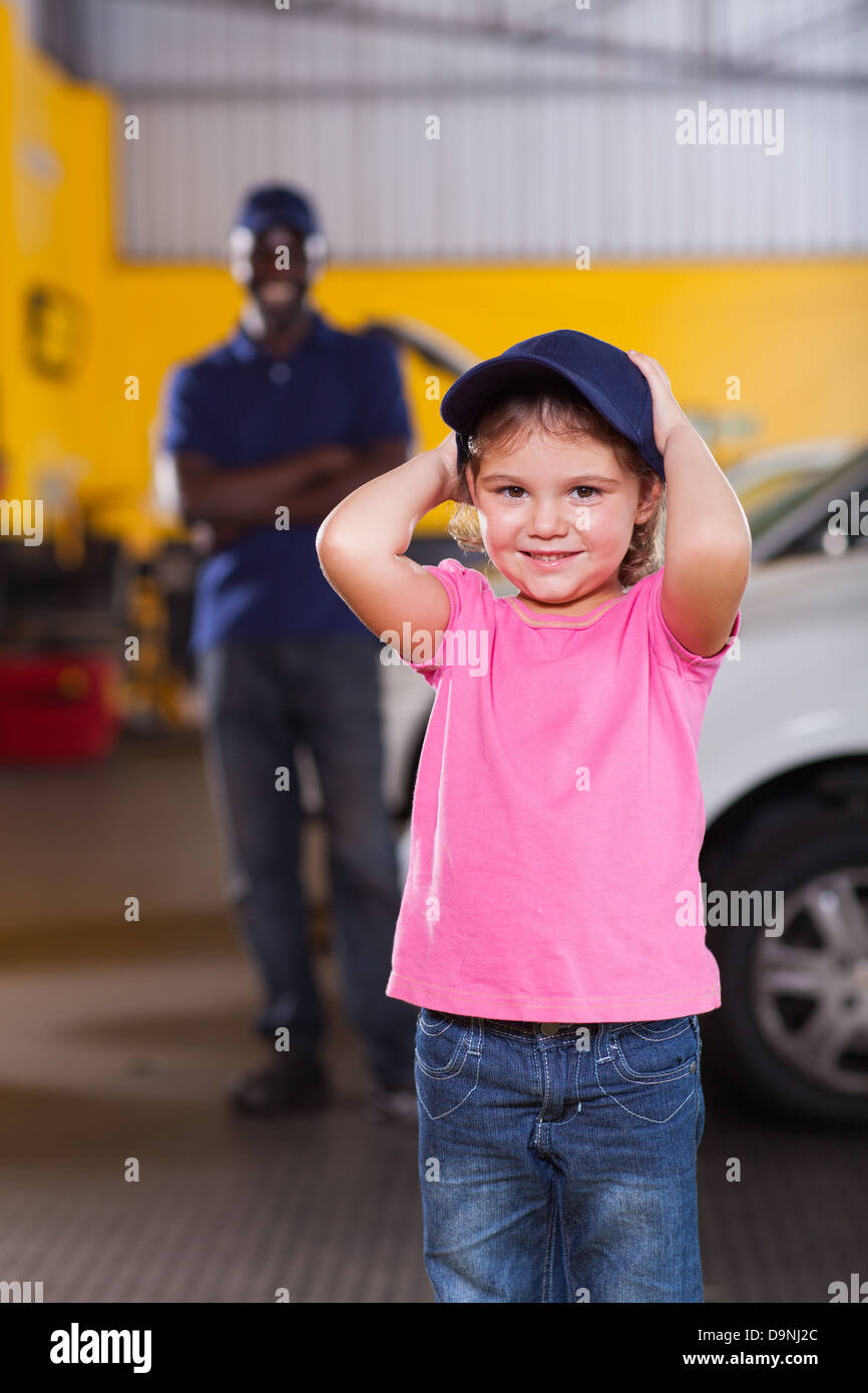 cute little girl wearing auto mechanic's cap in repair shop Stock Photo