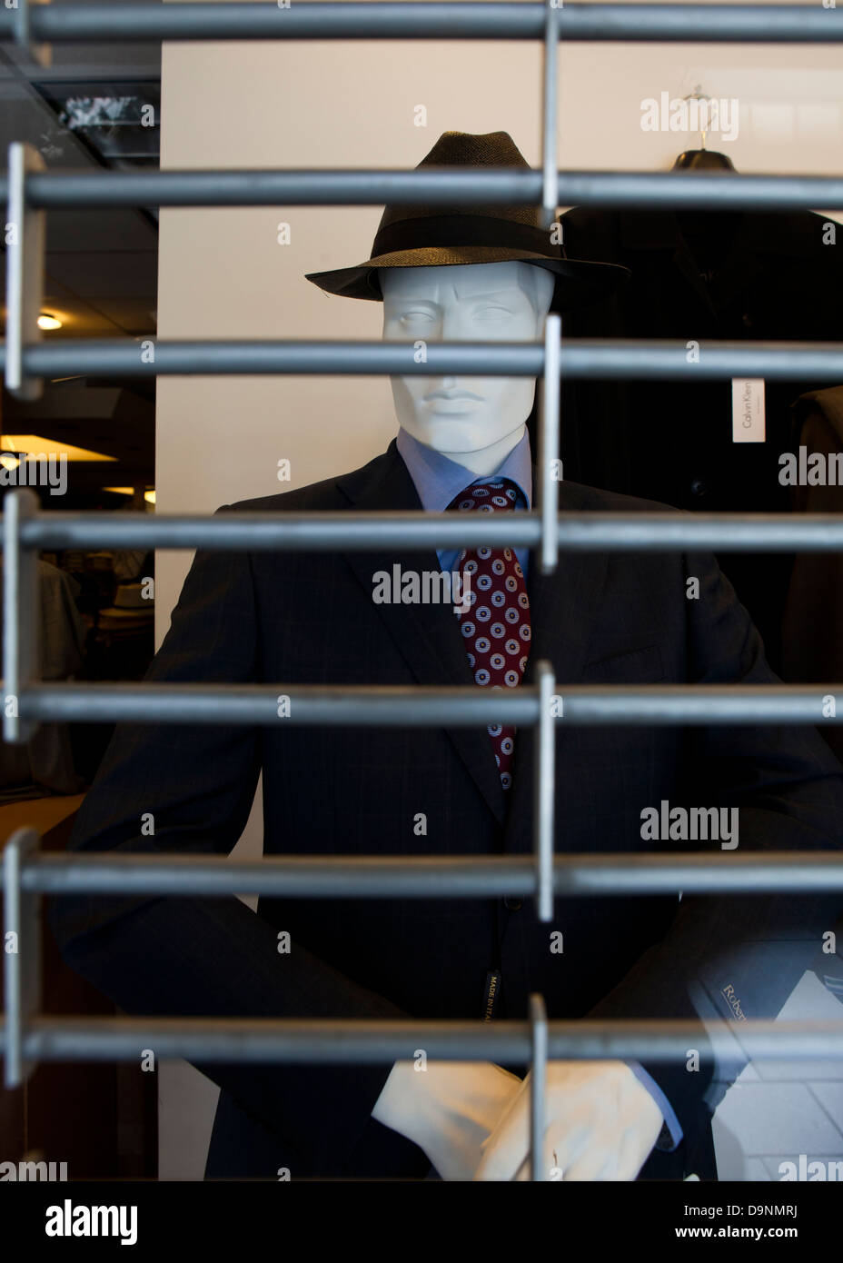 Men's business attire on mannequin behind barred shutter Stock Photo