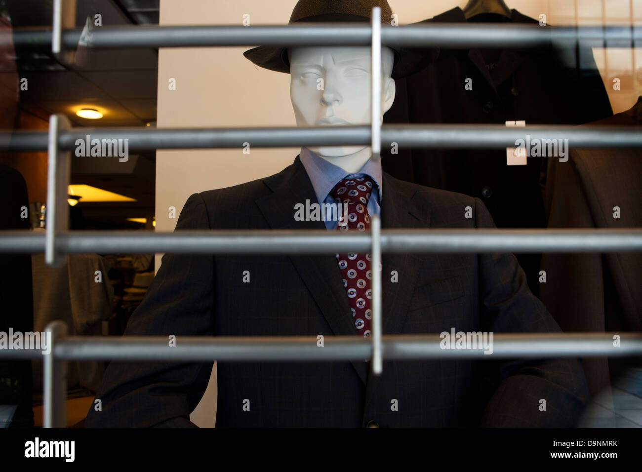 Men's business attire on mannequin behind barred shutter Stock Photo