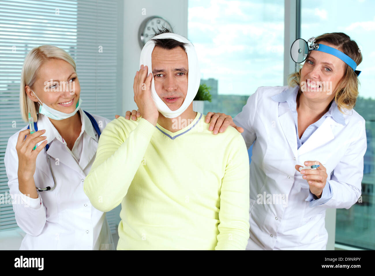 Portrait of two careful female doctors giving first aid to male patient with toothache in hospital Stock Photo