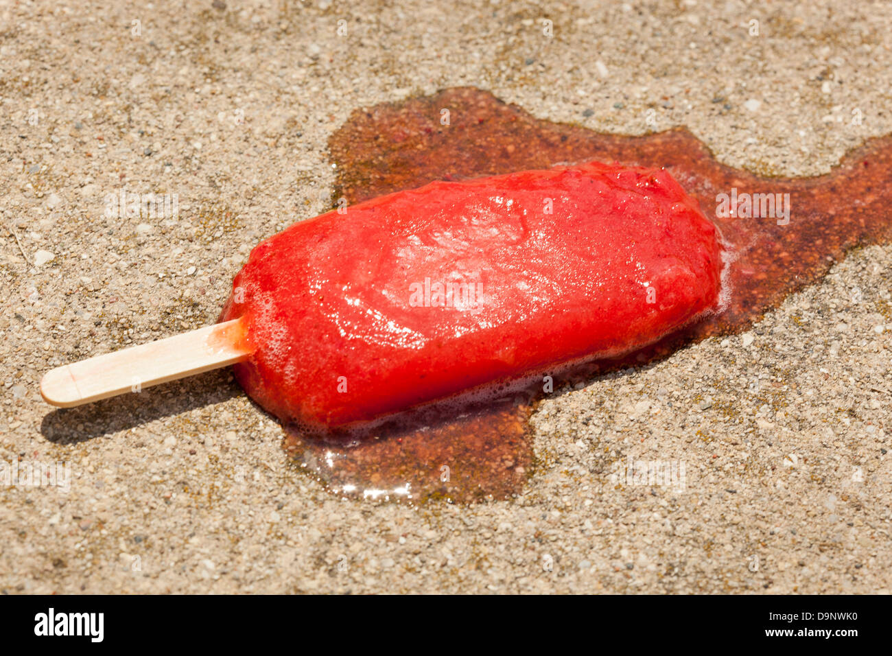 Cold Organic Frozen Strawberry Fruit Popsicle melted on the Ground Stock Photo