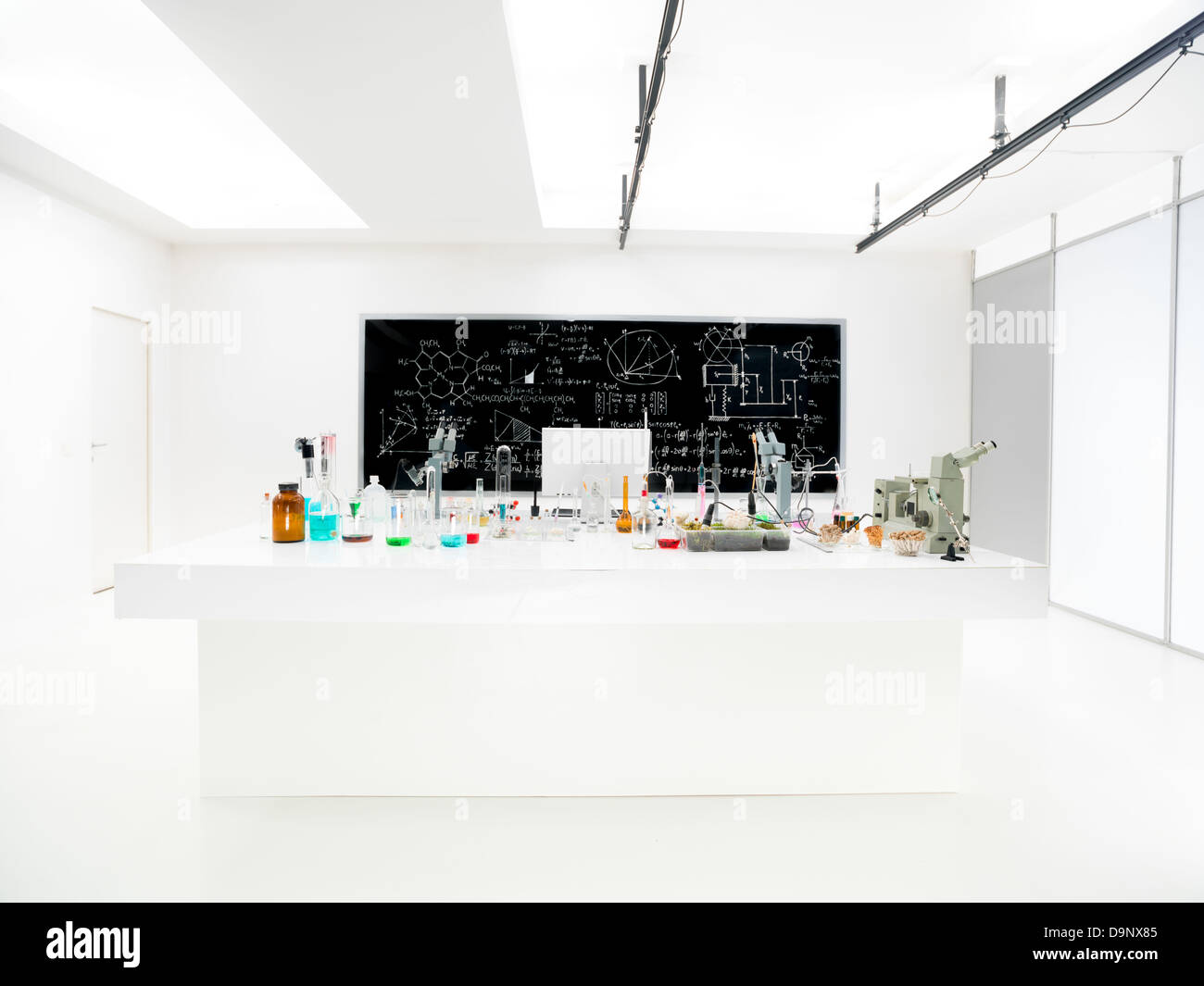 general-view of a chemistry laboratory with a lab table containing colorful liquids and lab tools and a blackboard on the background Stock Photo
