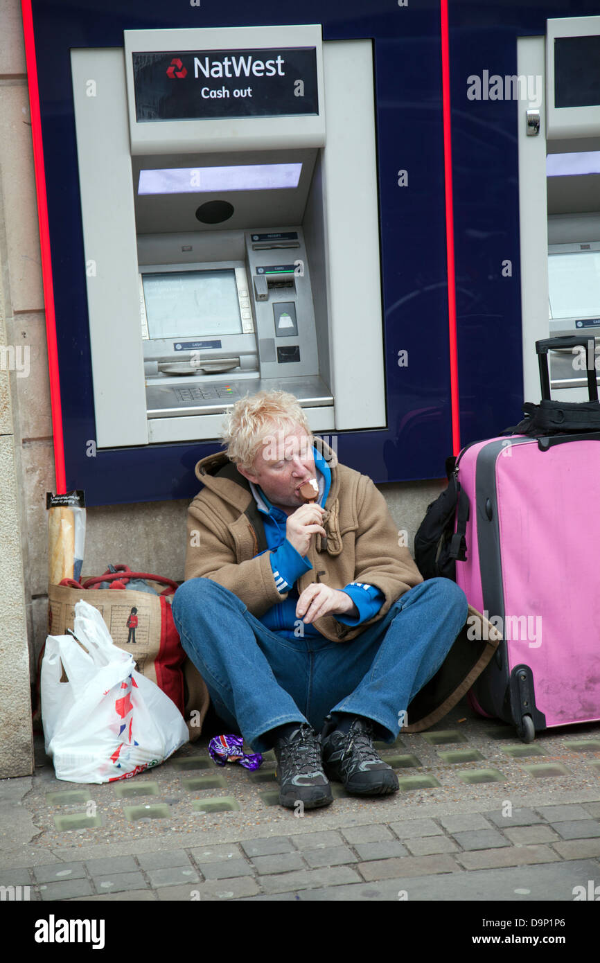 Homeless man with belongings eating Ice Cream in front of Natwest ATM in London City - UK Stock Photo