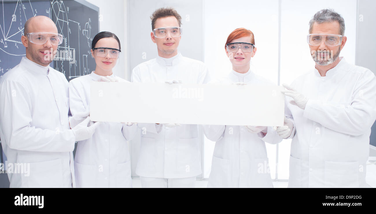 close-up of five scientists in a chemistry lab holding in hands an empty banner and confident looking in the camera with a black Stock Photo