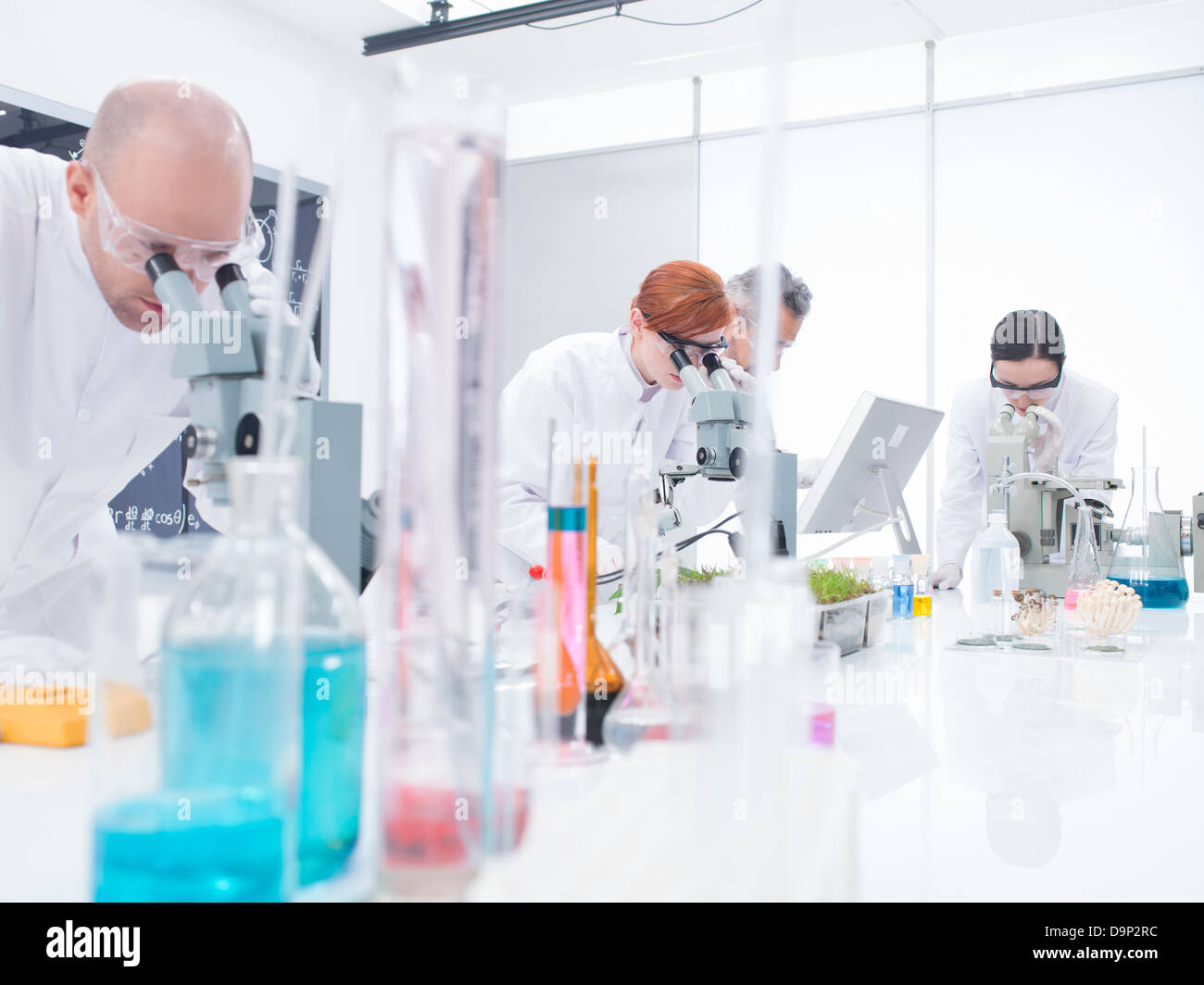general-view of people in chemistry lab analyzing under microscope on a lab table with colorful liquids and lab tools Stock Photo