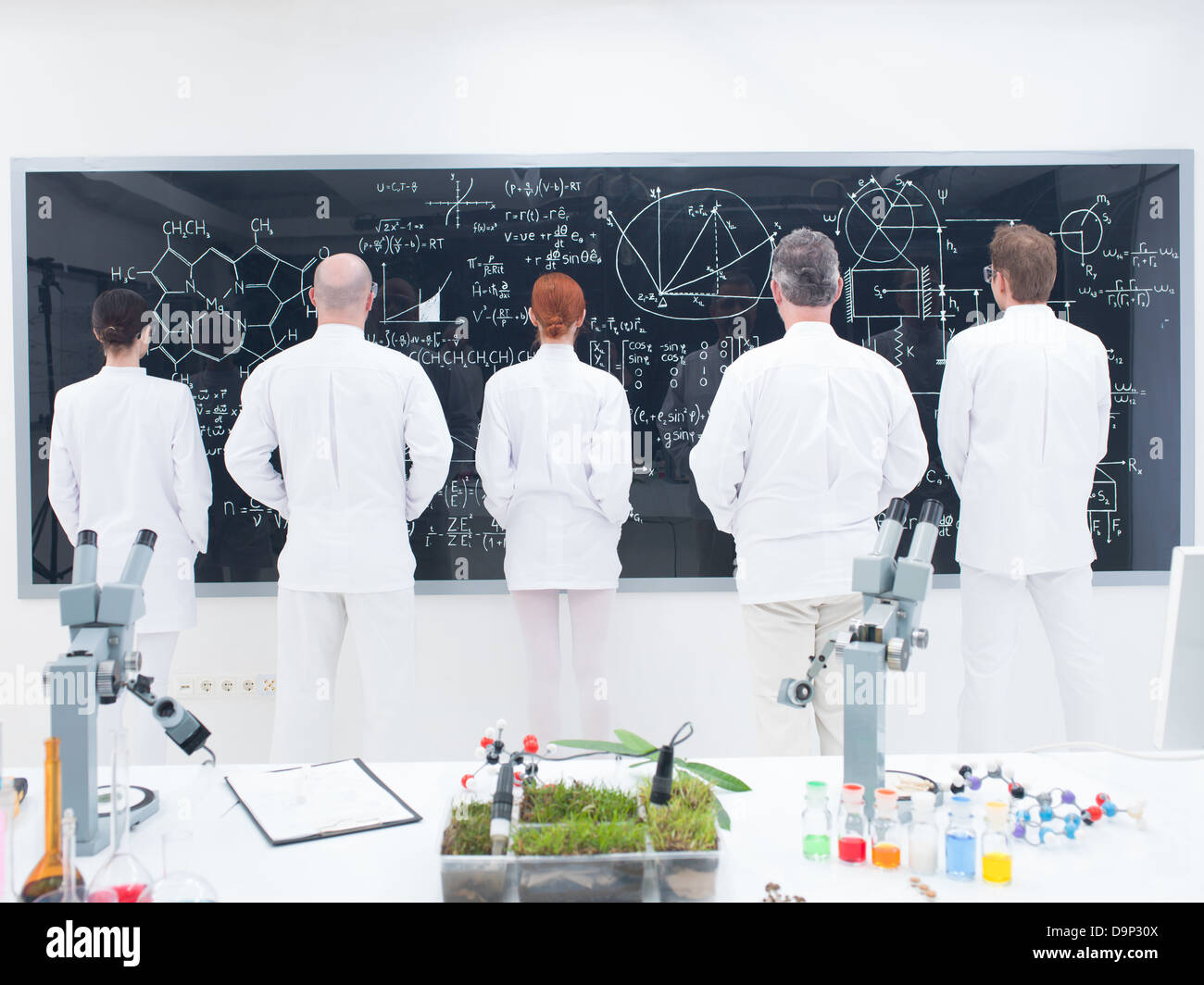 general-view of five scientists in a chemistry lab in front of a blackboard analyzing formulas on a blackboard Stock Photo