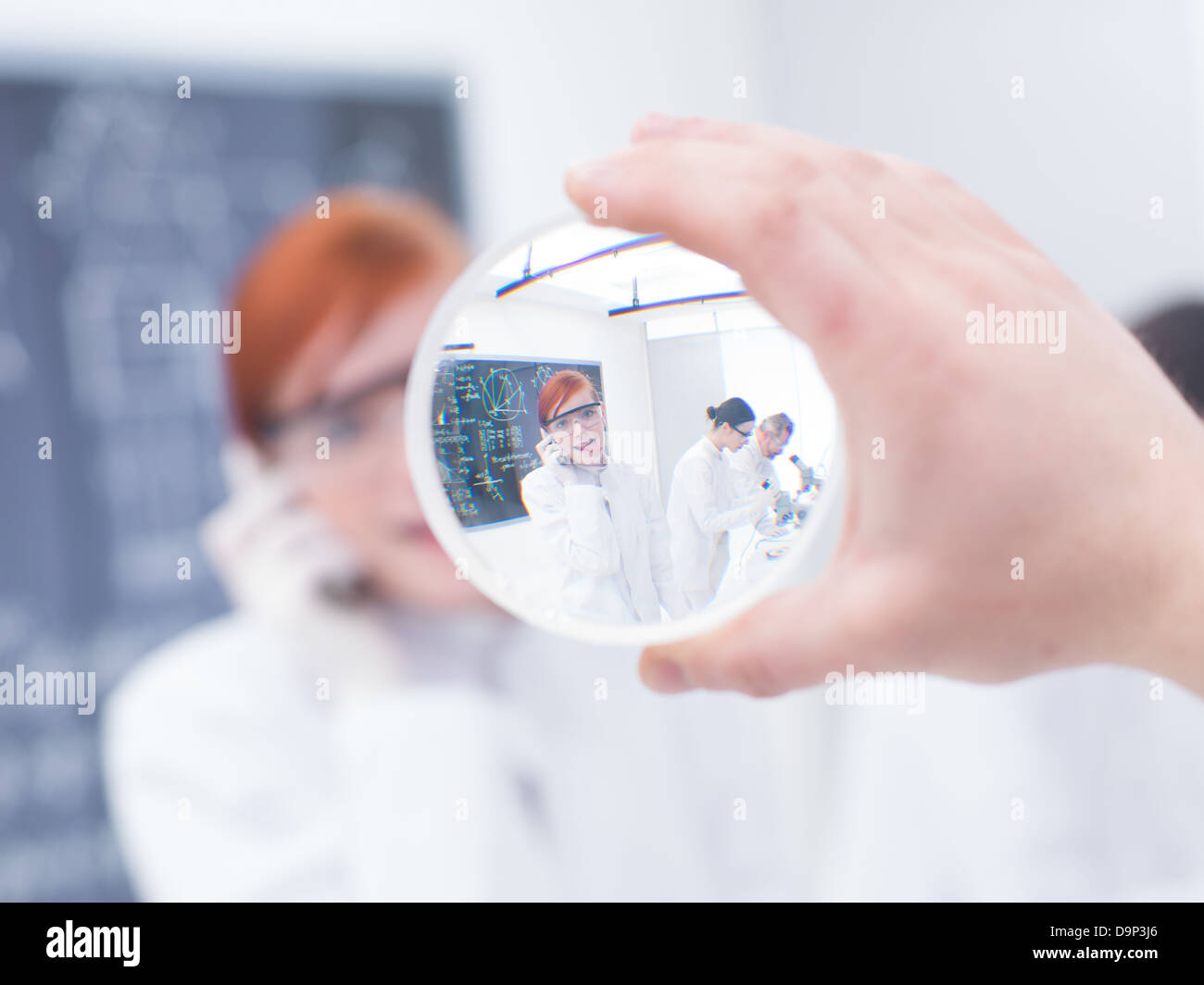 close-up of a beautiful student in a chemistry lab having fun and looking through a magnifier Stock Photo