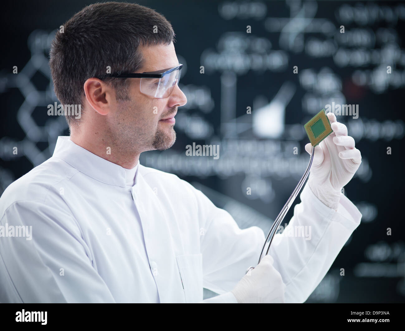 close-up of scientist in a chemistry lab holding in hands and analyzing a hard disk and a blackboard on the background Stock Photo