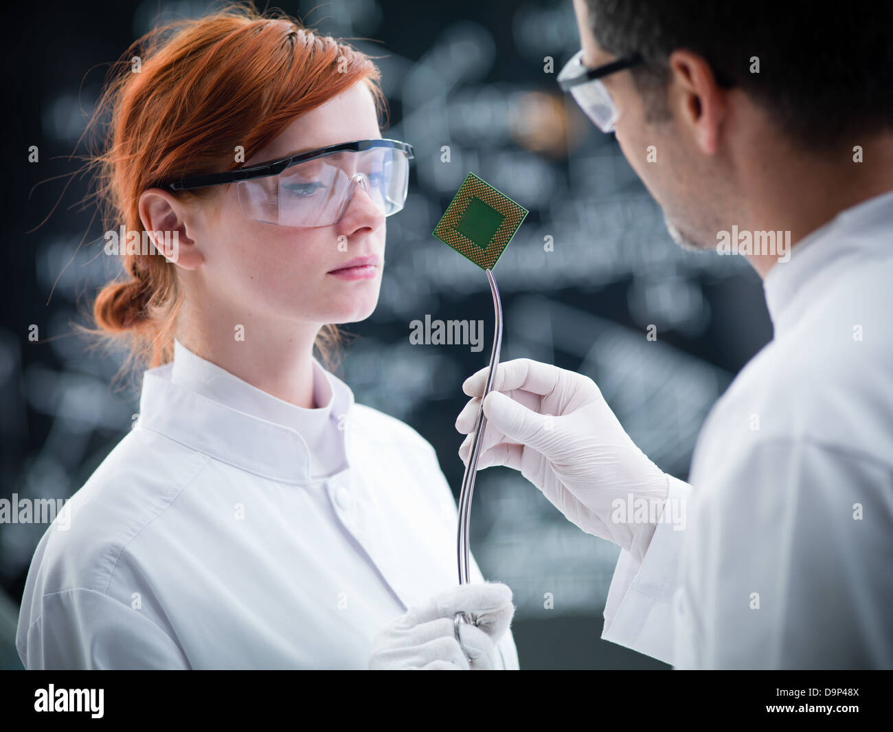 close-up of scientist in a chemistry lab holding in hands andshowing to a student a hard disk and a blackboard on the background Stock Photo