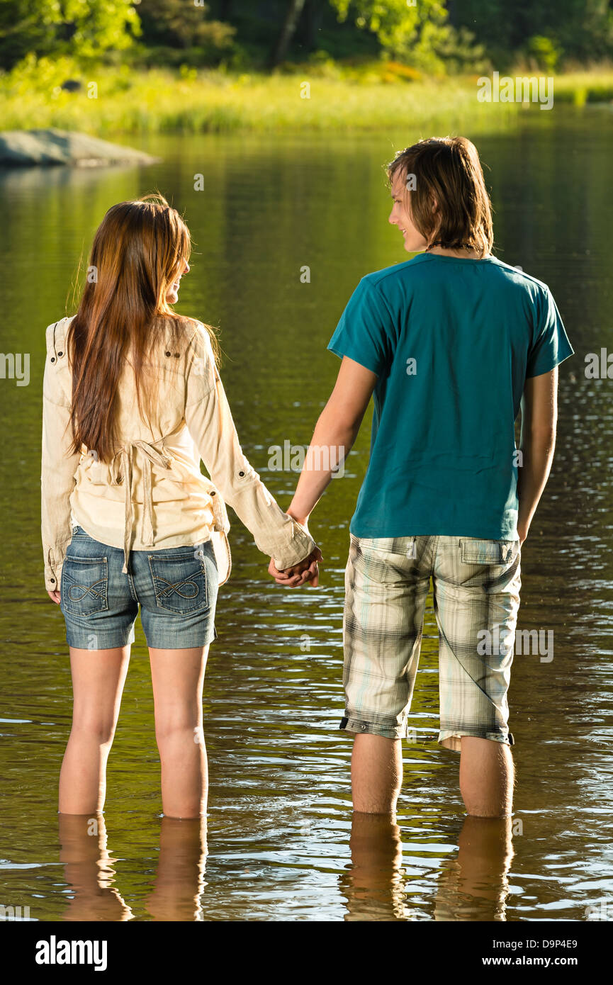 Teenage couple holding hands standing in water sunset by lake Stock Photo