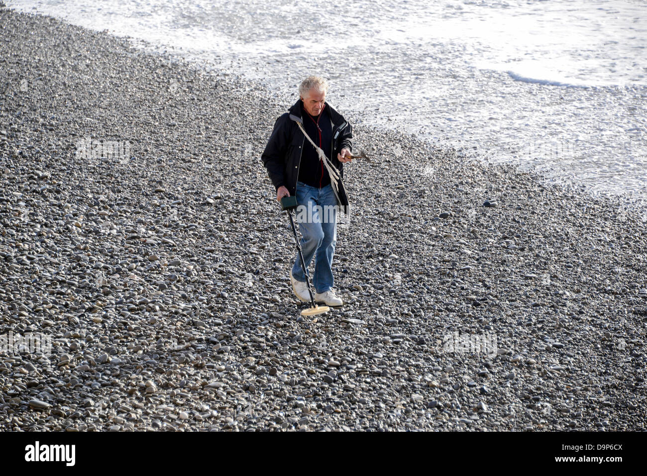 A man with a metal detector combs the beach at Nice France in December Stock Photo
