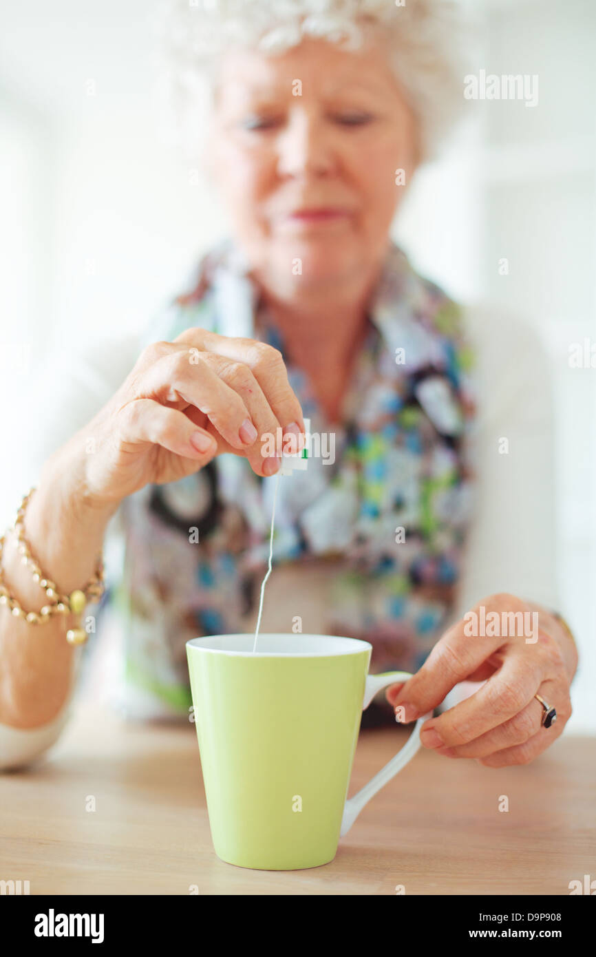 Old lady sitting at home holding and dipping a tea bag Stock Photo