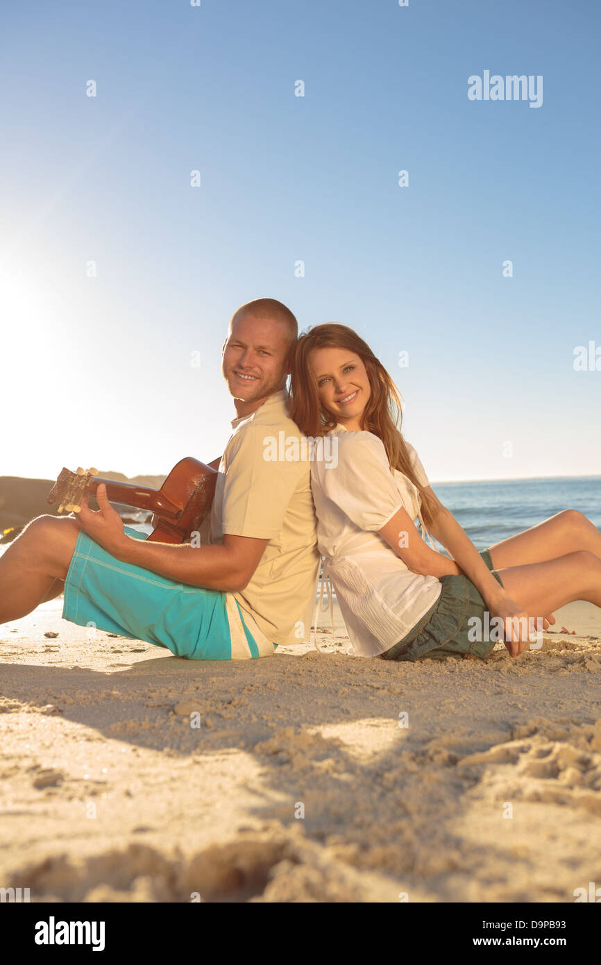 Young couple sat back-to-back on the beach Stock Photo