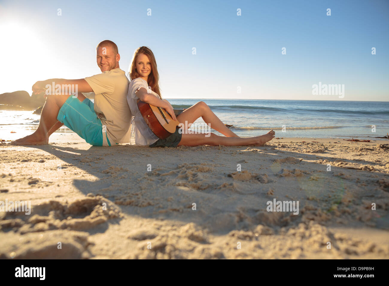 Happy couple sat back-to-back on the beach Stock Photo