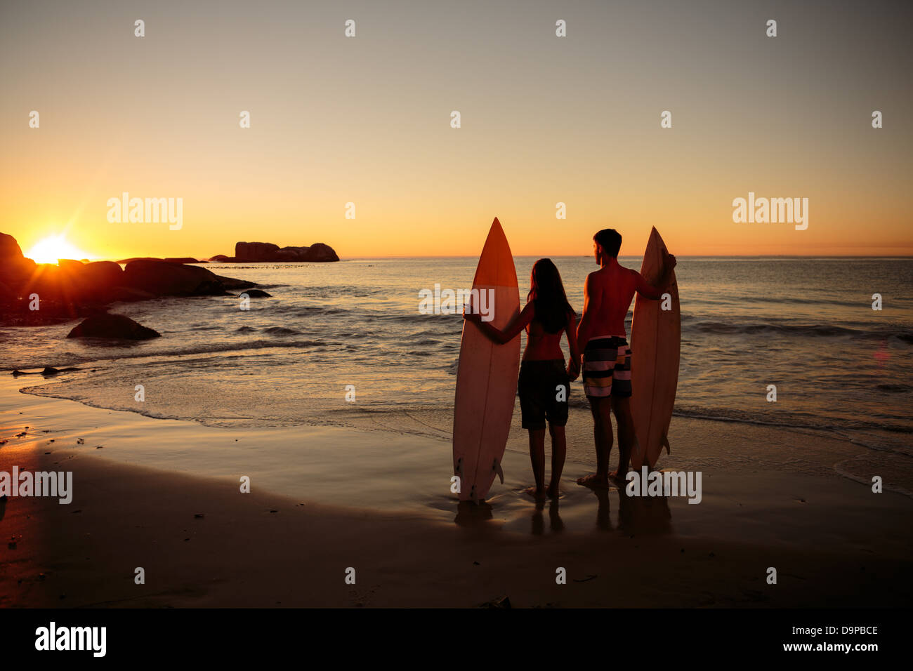 Lovers hand in hand with surfboards looking at the sunset Stock Photo