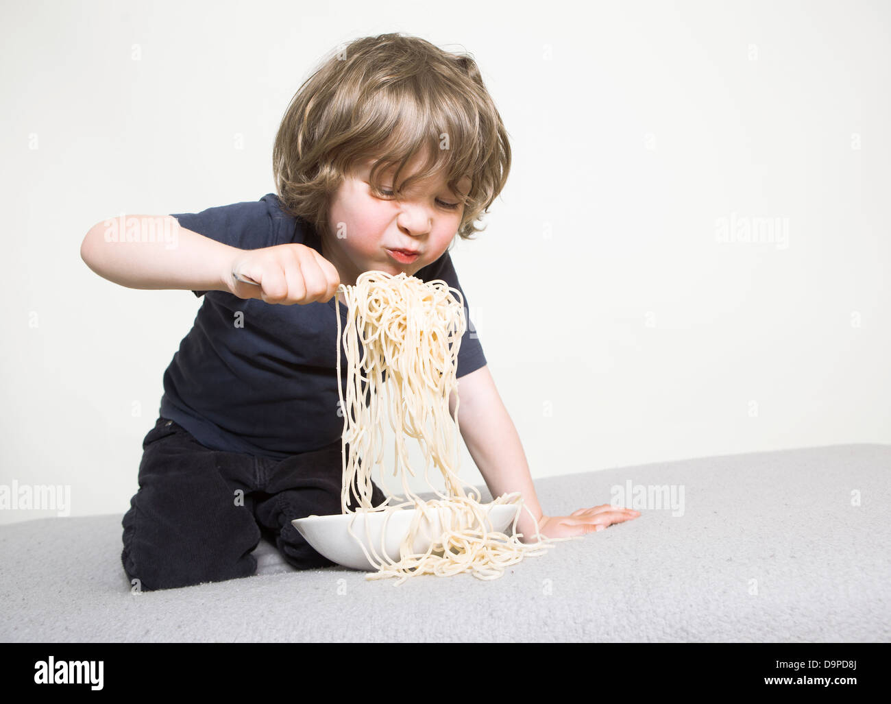 young boy eating his pasta on the couch Stock Photo