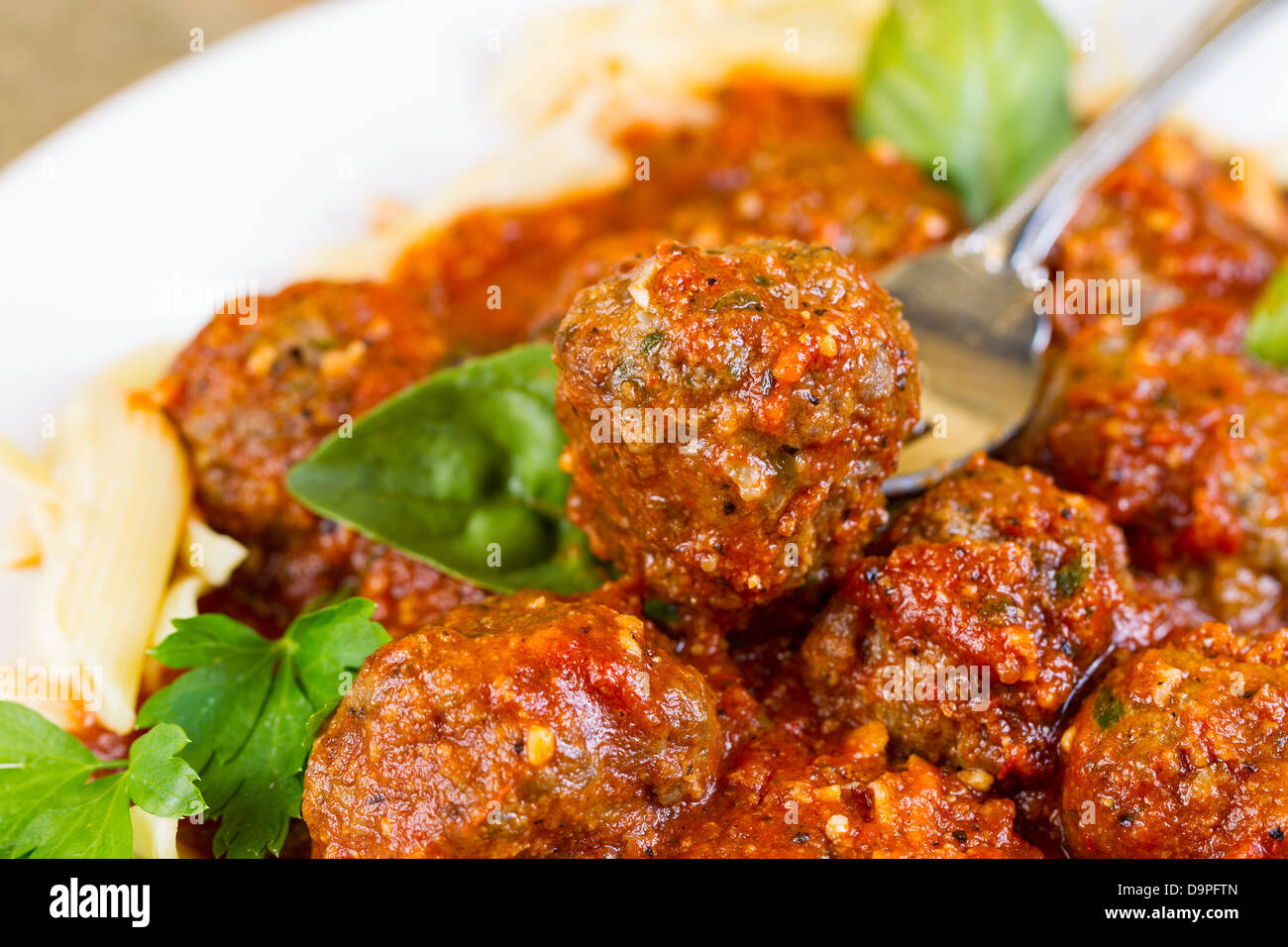 Horizontal photo of bread coated cooked meatball in fork with, pasta