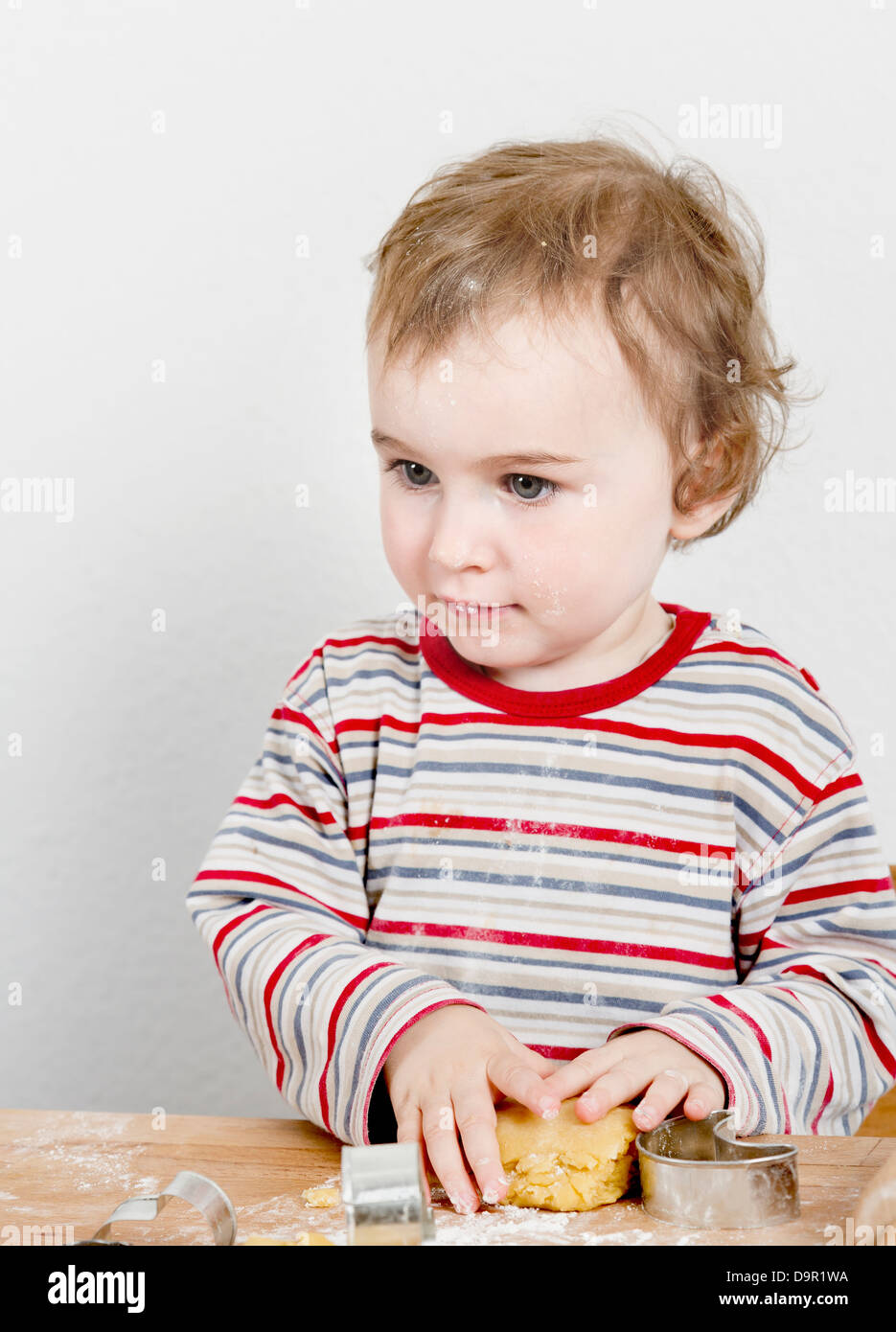 vertical image of 2 year old child making biscuit at wooden desk Stock Photo