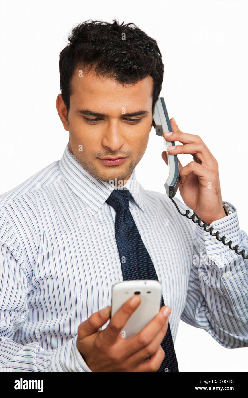 Businessman talking on a landline phone while looking at a mobile Stock Photo