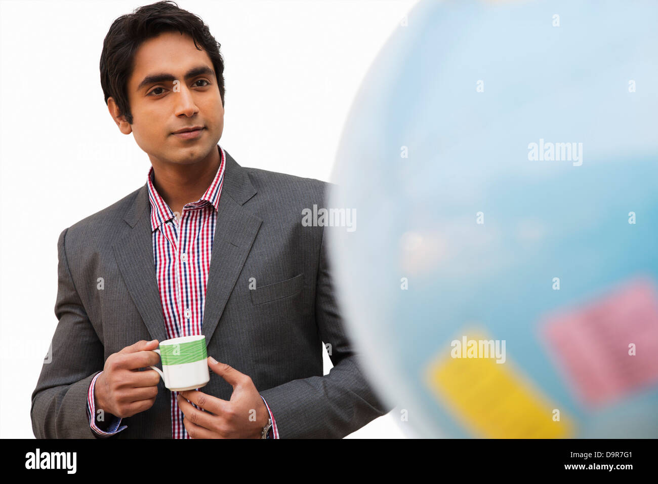 Businessman holding a tea cup and looking at a globe Stock Photo