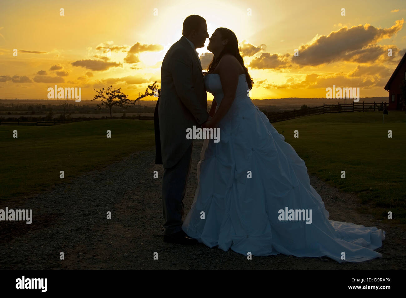 Horizontal close up portrait of a bride and groom holding hands together infront of a romantic sunset on their wedding day. Stock Photo