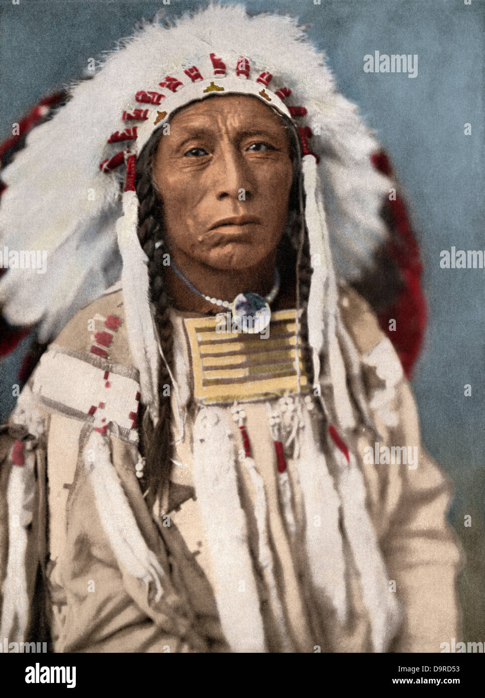 Crow Indian chief in a traditional war bonnet and clothing, circa 1900. Hand-colored halftone of a photograph Stock Photo