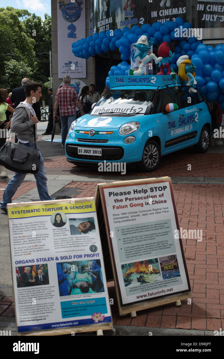 Promotional car with figurines of 3 Smurfs on its roof stands in front of St. Stephen's Green Shopping Centre, Dublin, Ireland. Promo activities were related to the latest Smurfs movie. Posters of Falun Gong organization in the foreground. Stock Photo