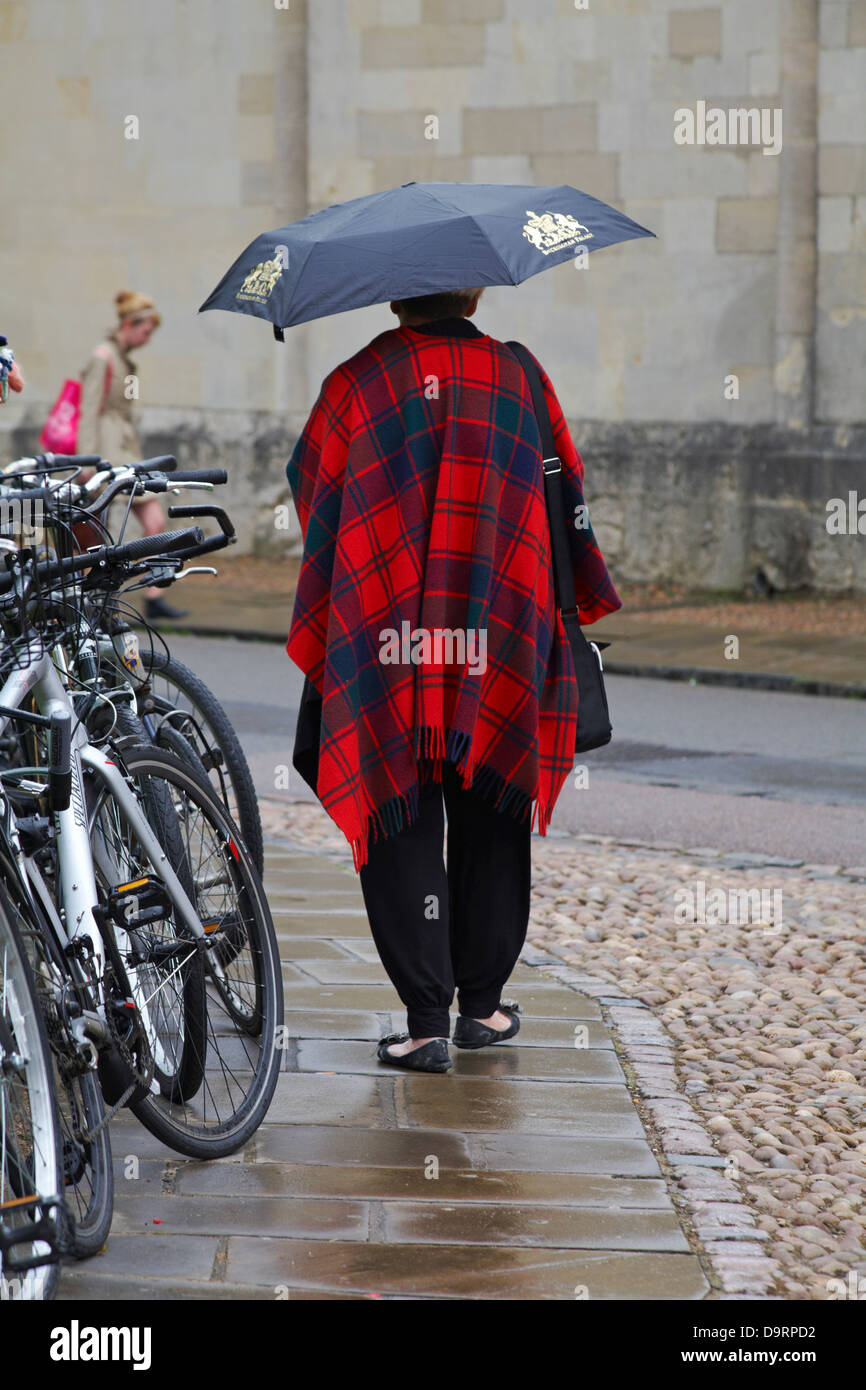 woman wearing checked cape and sheltering under Buckingham Palace umbrella in the rain at Oxford, Oxfordshire UK on a wet rainy day in May Stock Photo