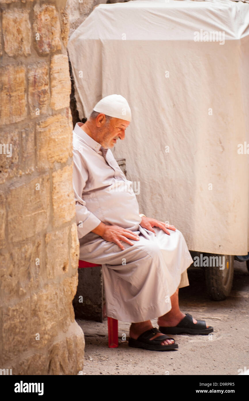 Israel Jerusalem Old City Muslim Arab Quarter old elderly man seated sitting napping wearing white skullcap grey robe thwarb thobe Stock Photo