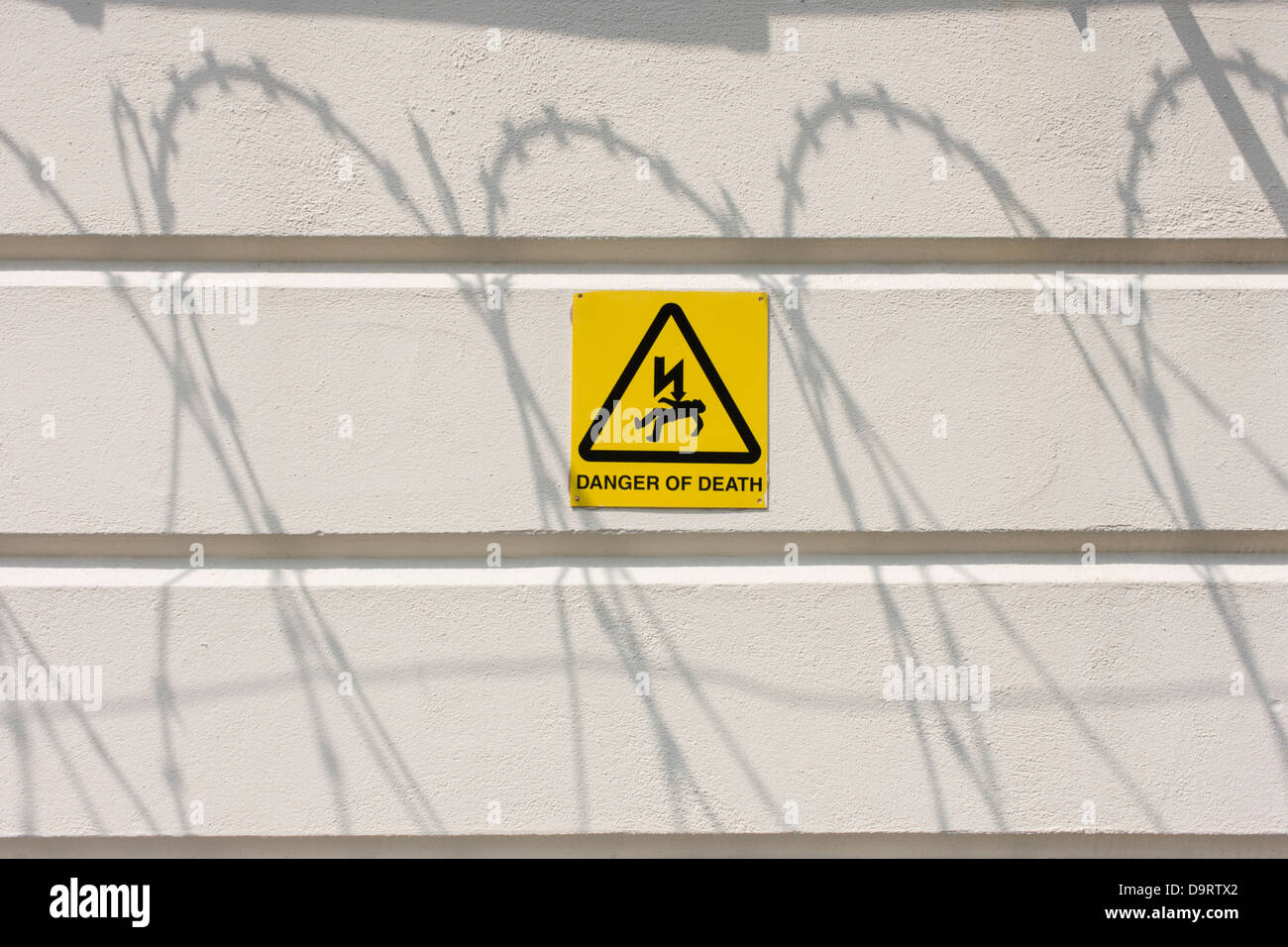 Shadows of razor-wire with a Danger of Death sign, on a white perimeter wall of the All England Lawn Tennis Club, Wimbledon. Stock Photo