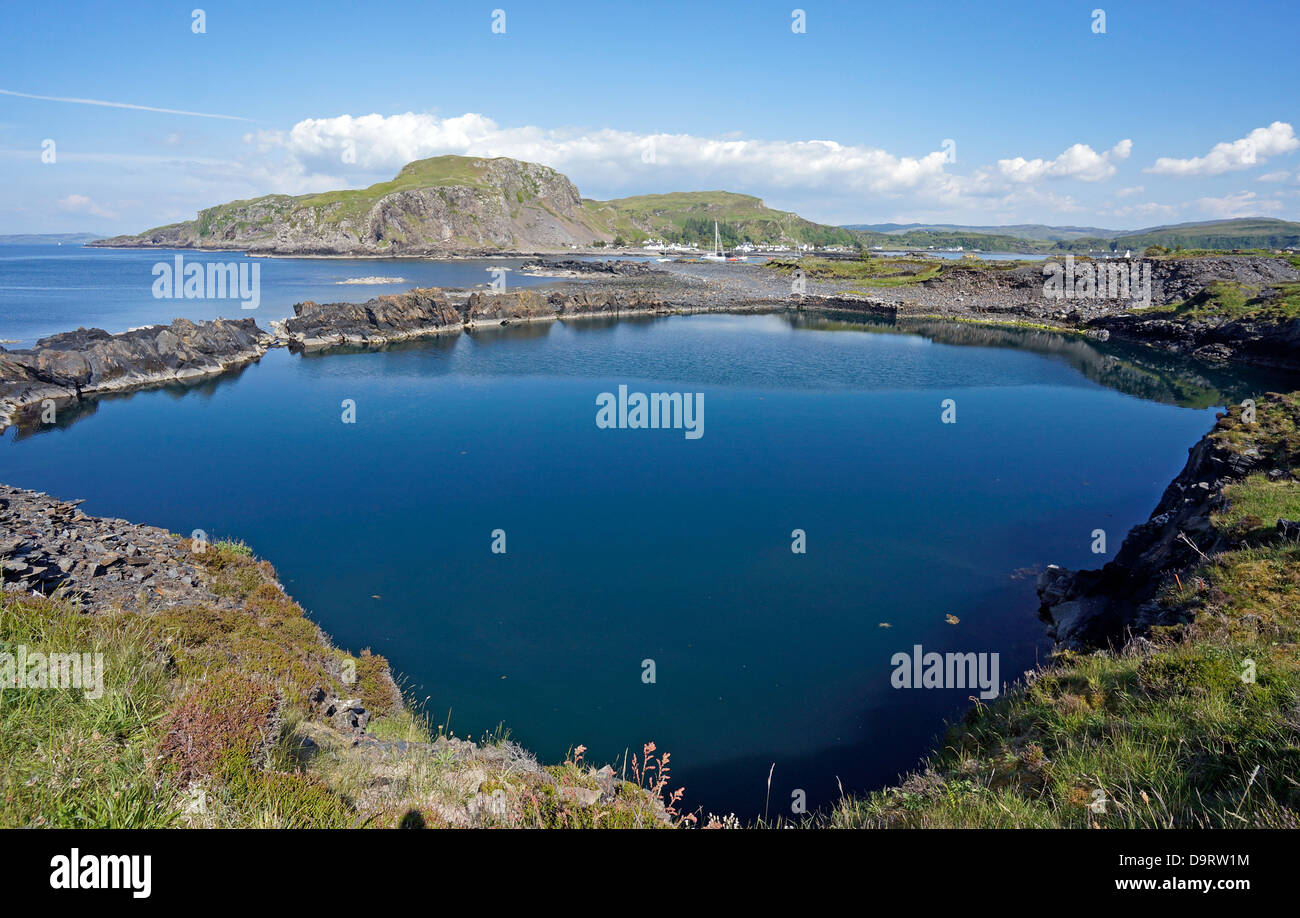 Flooded & disused slate quarry on island of Easdale in western Scotland with the village of Easdale on Seil in the background Stock Photo