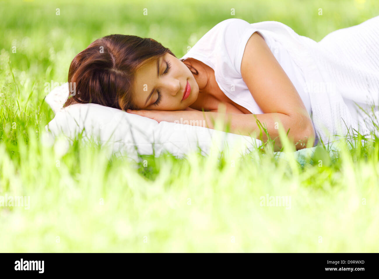 Young woman sleeping on soft pillow in fresh spring grass Stock Photo