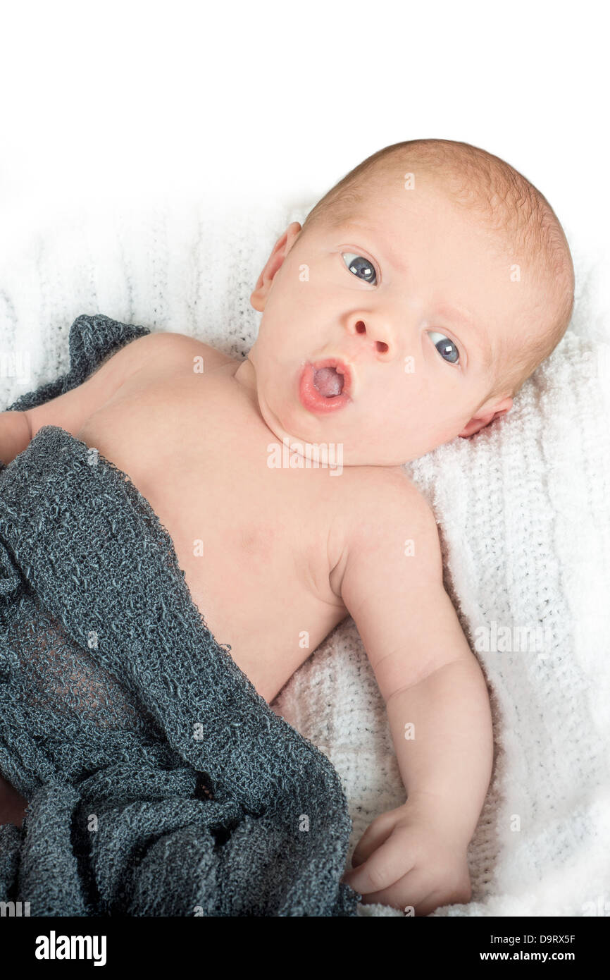 Awake baby with surprised look on his face and blue eyes lying on a white blanket Stock Photo