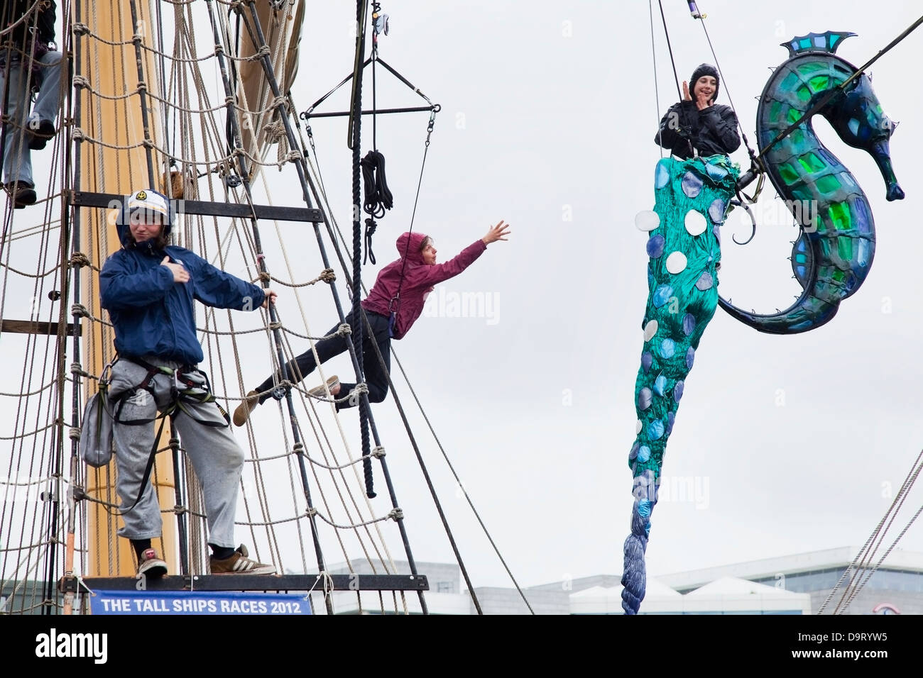 Three people hanging from harnesses on a ship for the tall ship race