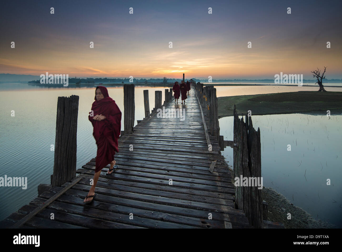 monks crossing U Bein Bridge at dawn, nr Mandalay, Myanmar (Burma) Stock Photo