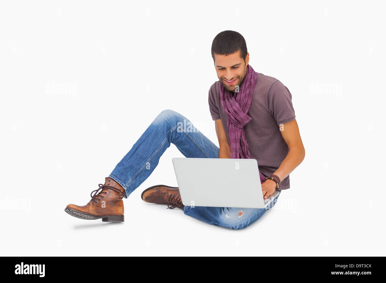 Smiling man wearing scarf sitting on floor using laptop Stock Photo