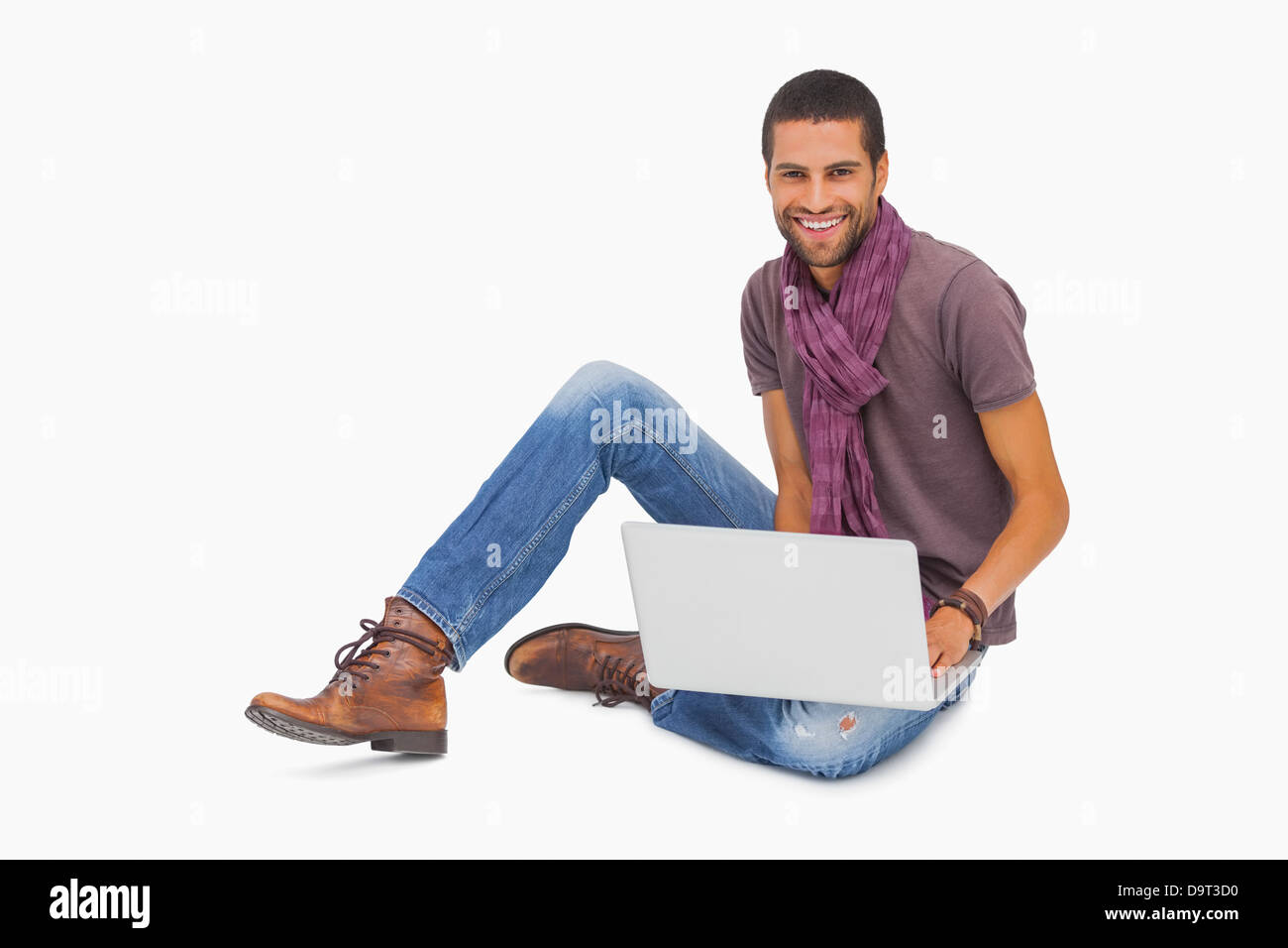 Happy man wearing scarf sitting on floor using laptop Stock Photo