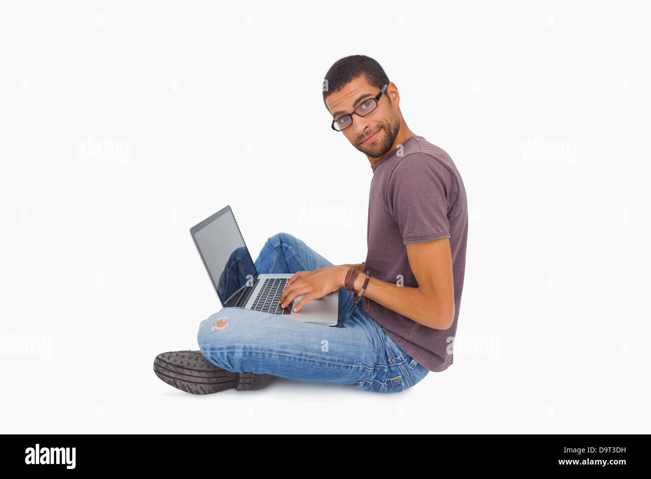 Man wearing glasses sitting on floor using laptop and looking at camera Stock Photo