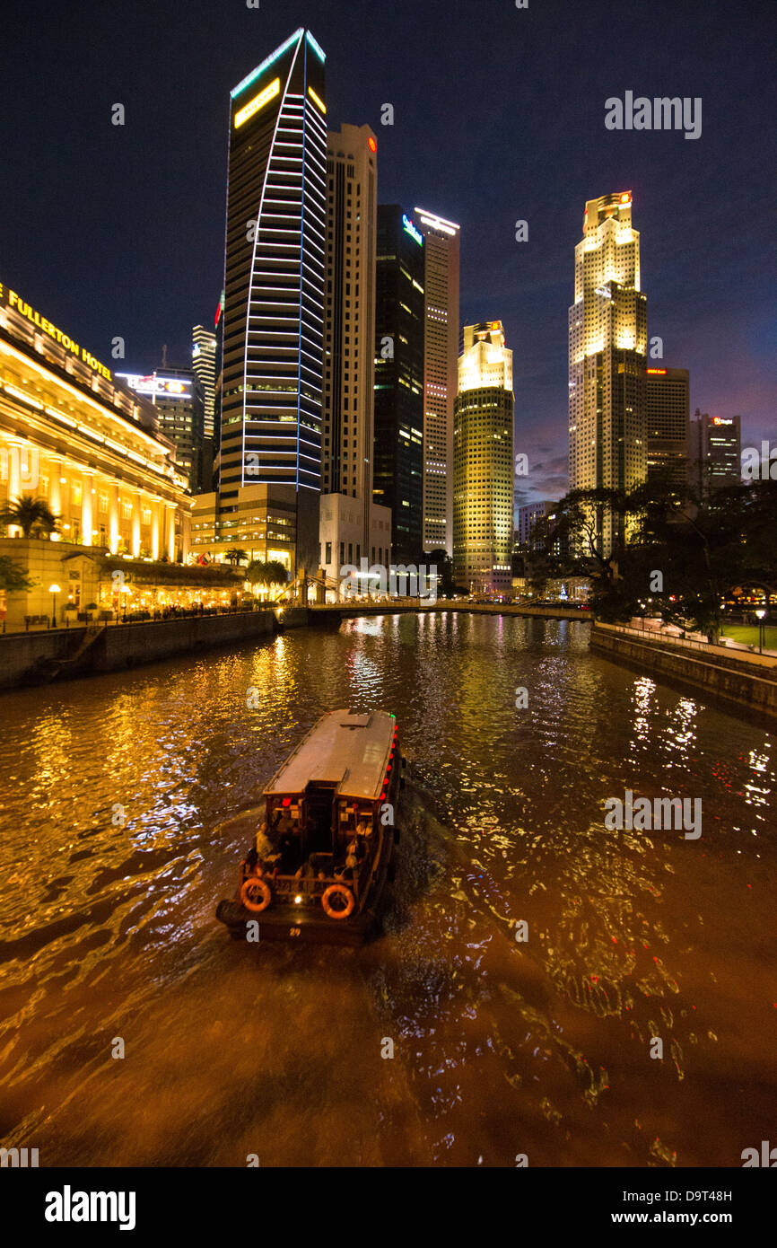 the Cavenagh Bridge, a boat on the Singapore River, the Fullerton Hotel and Central Business District at night, Singapore Stock Photo