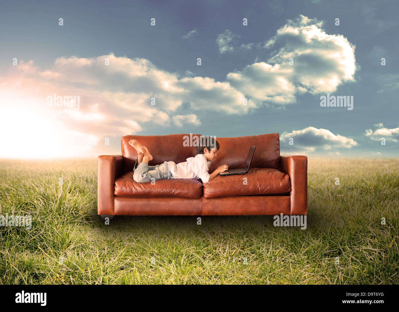 Child using laptop on couch in field Stock Photo